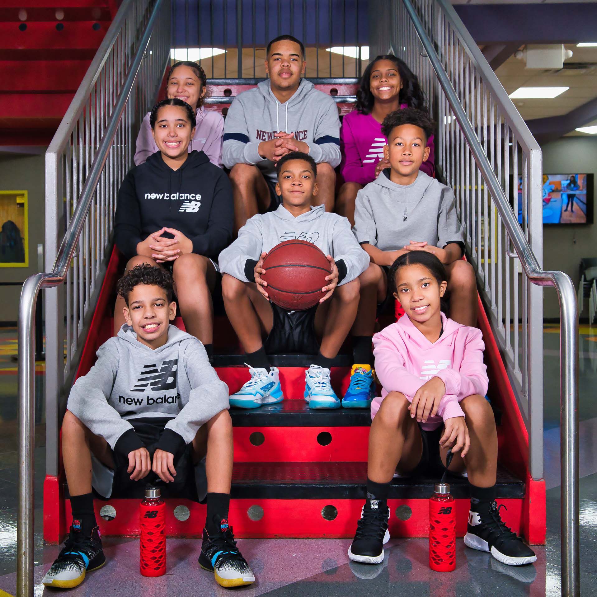 Group of kids sitting on staircase wearing New Balance gear with boy holding basketball