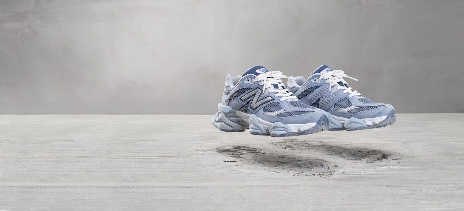 A pair of grey New Balance 9060 sneakers floating in the air above a lunar inspired background.