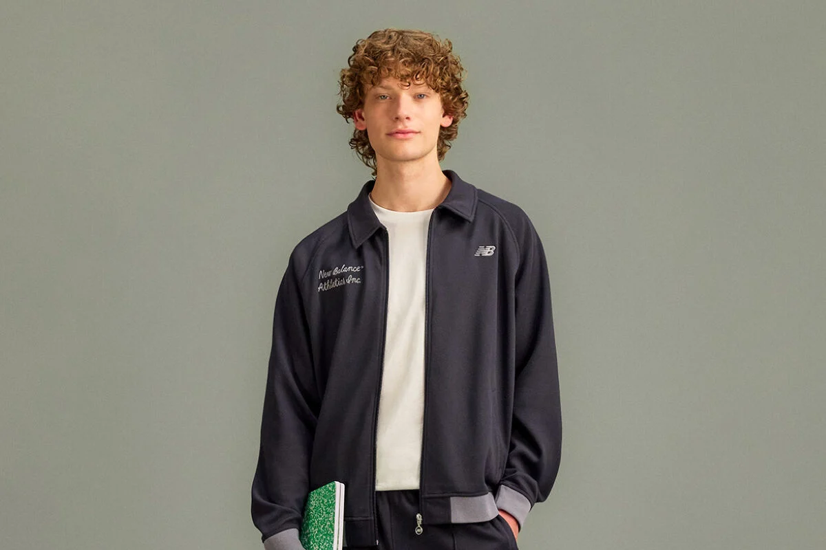 he person is wearing a dark zip-up jacket with a small New Balance logo on the chest and embroidered text on the opposite side that reads &ldquo;New Balance Athletics Inc.&rdquo;