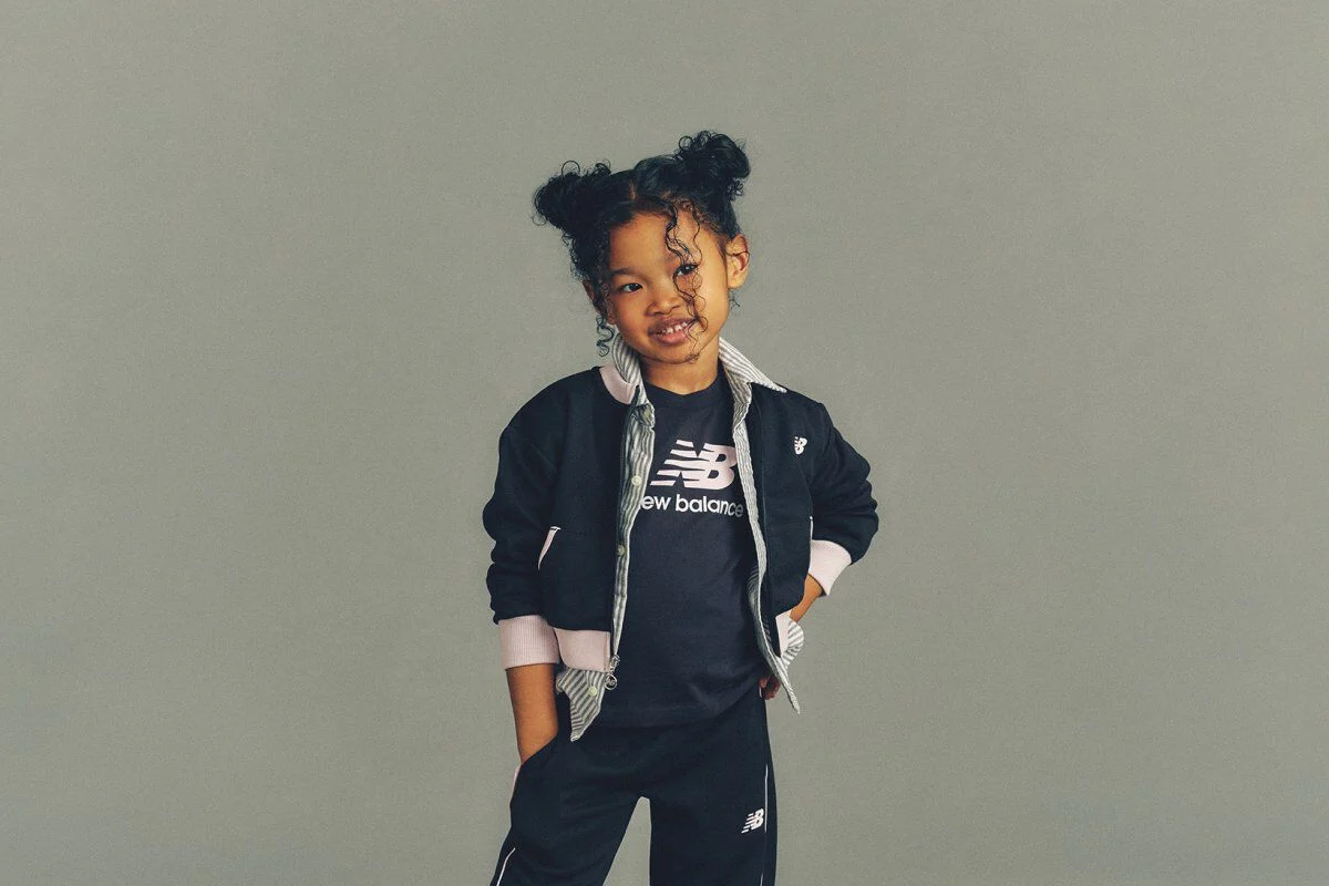 The child is wearing a black New Balance athletic outfit consisting of a logo T-shirt and matching jogger pants. 