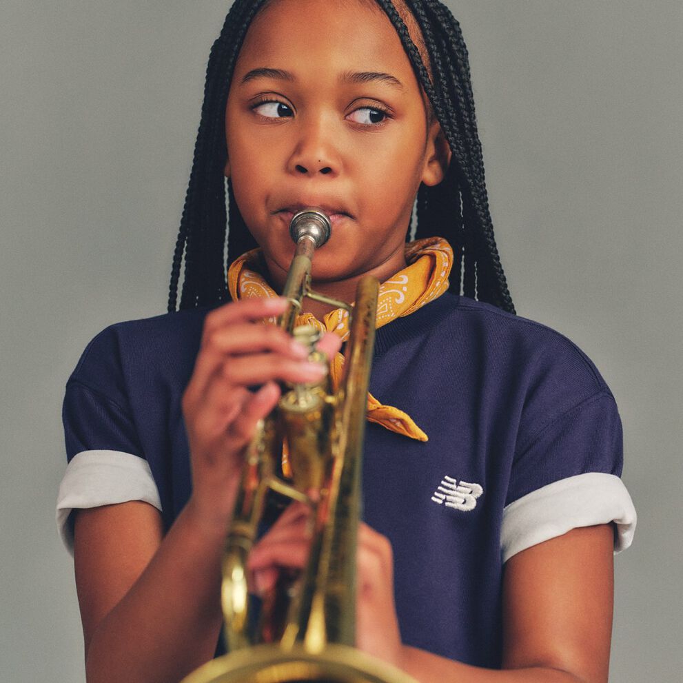 Close-up studio image of a child holding and playing a brass trumpet against a smooth, light gray background. 