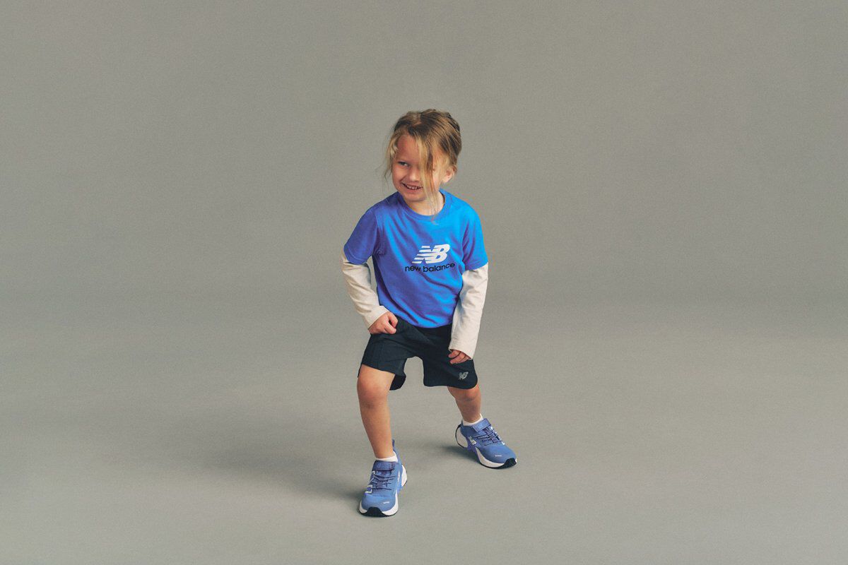 Close-up studio image of a child holding a blue, white, and purple soccer ball above the head with both hands.