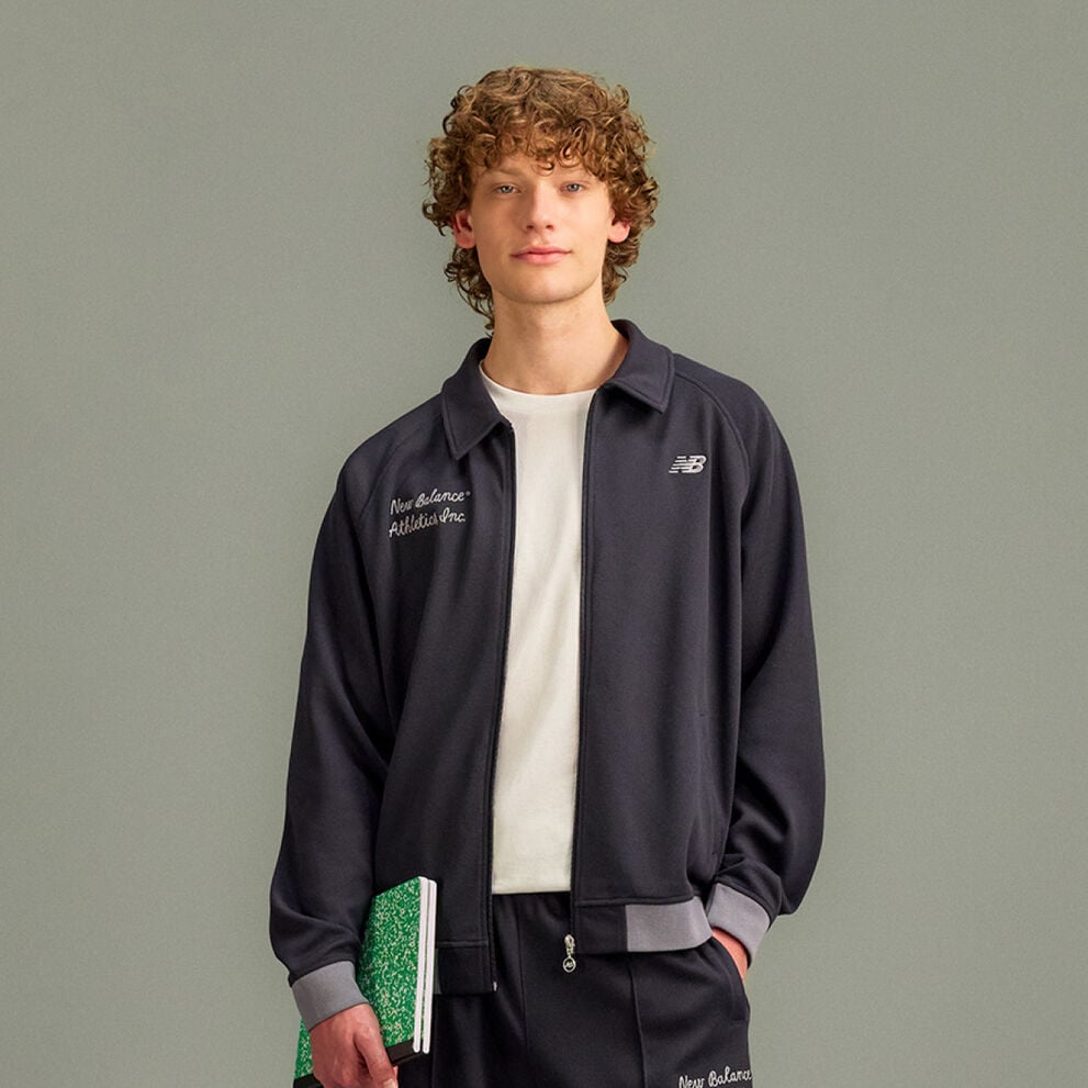 he person is wearing a dark zip-up jacket with a small New Balance logo on the chest and embroidered text on the opposite side that reads &ldquo;New Balance Athletics Inc.&rdquo;