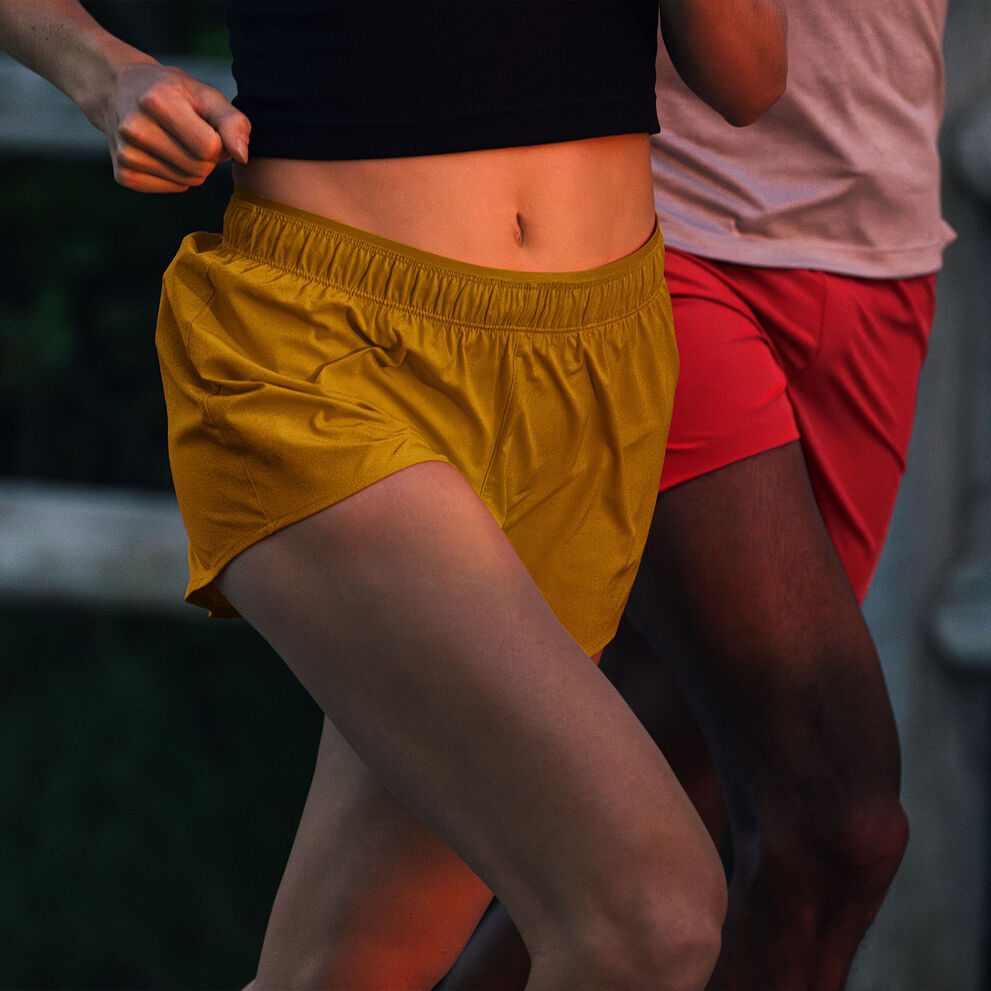 Two individuals running outside, wearing New Balance RC shorts.
