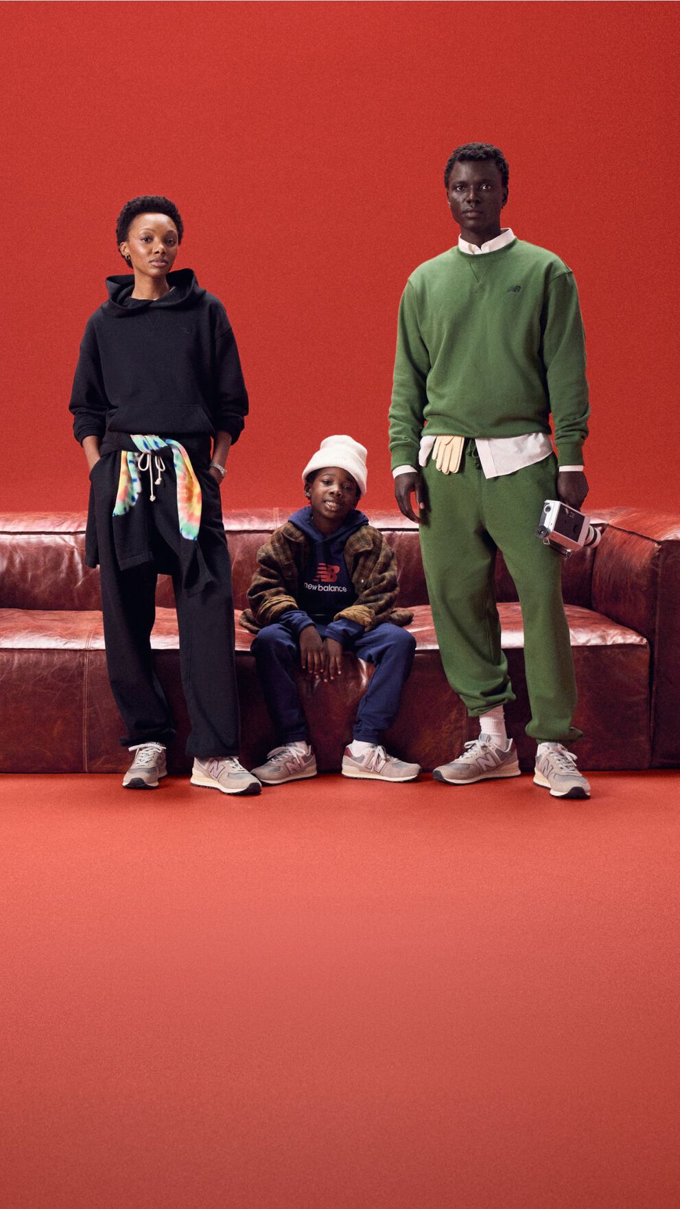 Family of three sitting on a red leather couch on a red background.