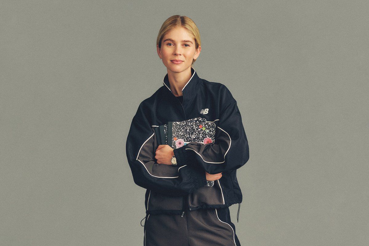 The person is wearing a black track jacket with light piping details and a small New Balance logo on the chest, paired with matching black pants.