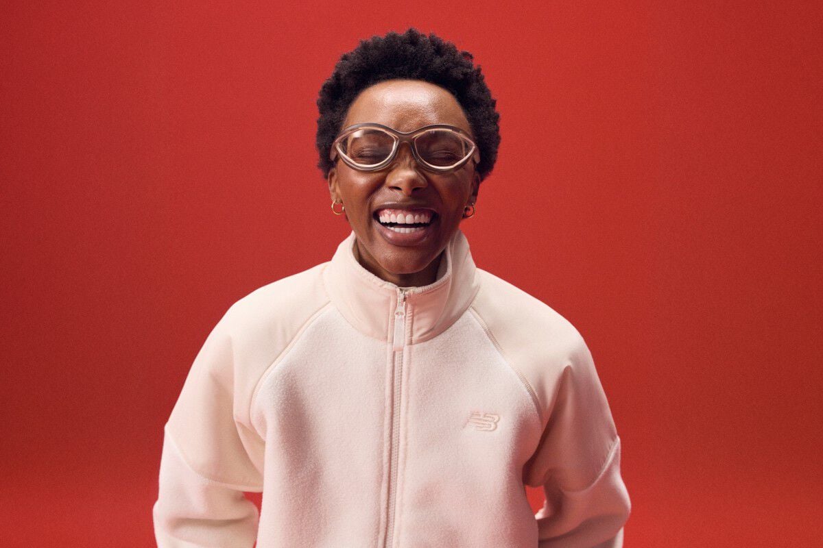 Woman laughing while wearing a pink zip-up on a red background.