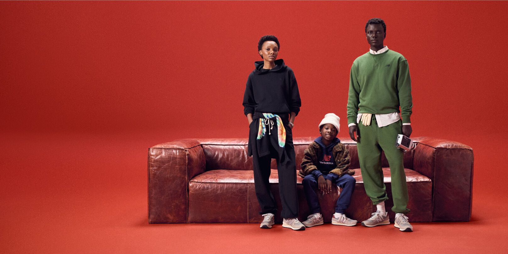 Family of three sitting on a red leather couch on a red background.