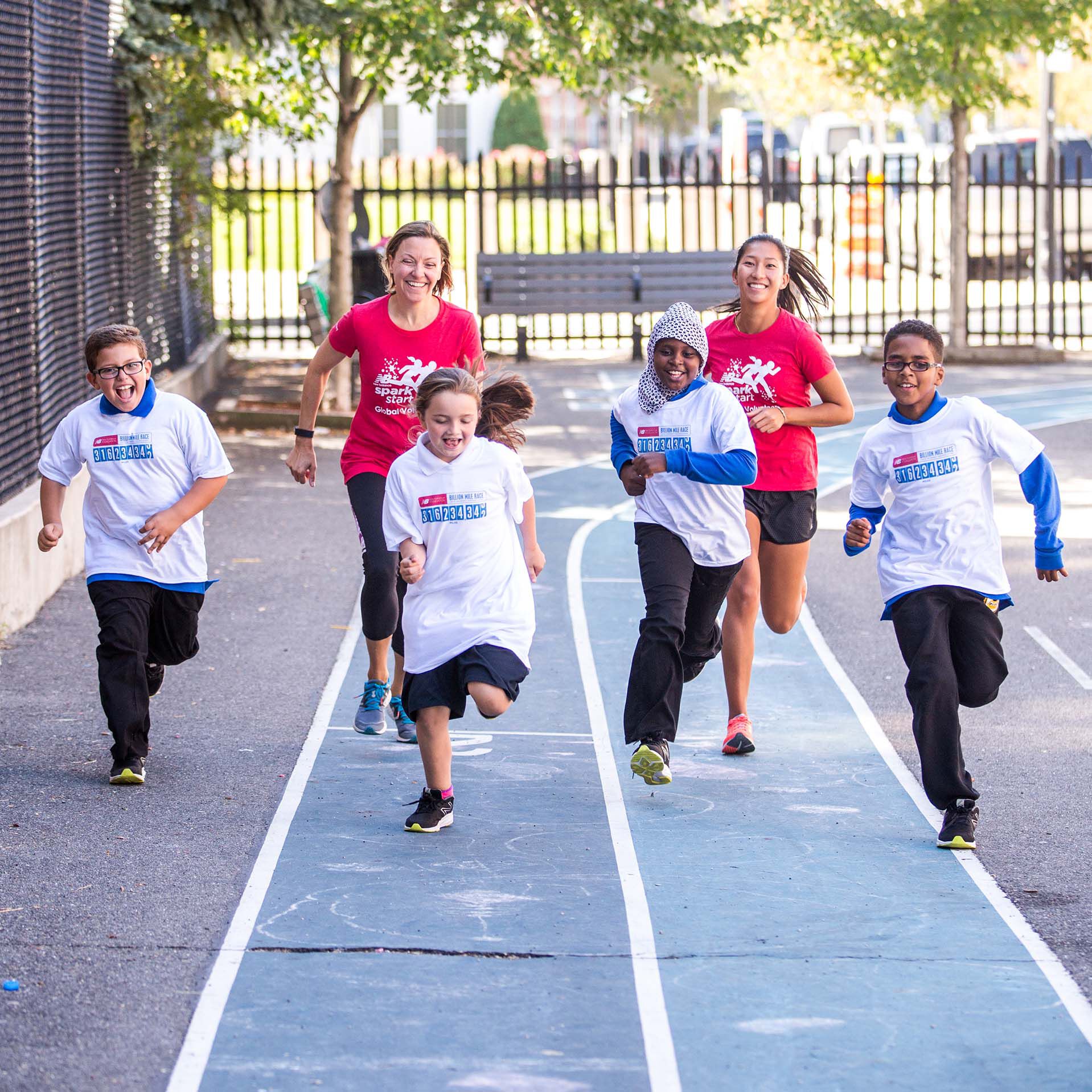 2 female New Balance employees smiling and running on outdoor track with kids