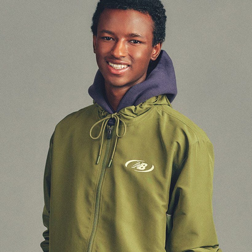 Close-up portrait of a person wearing a green New Balance jacket layered over a hoodie, standing against a plain background.
