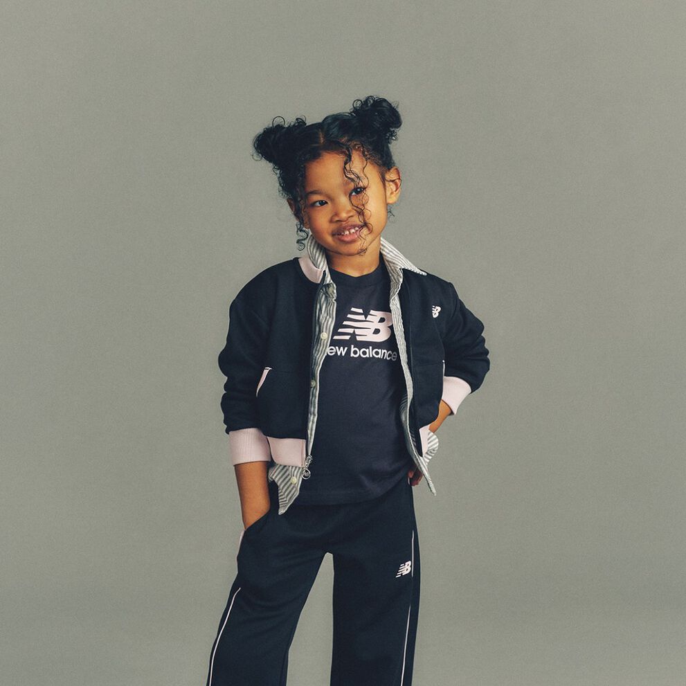 The child is wearing a black New Balance athletic outfit consisting of a logo T-shirt and matching jogger pants. 