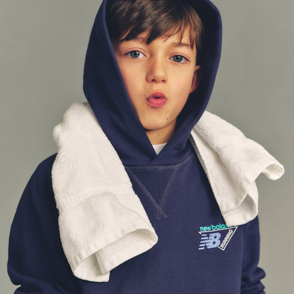 Close-up studio image of a child wearing a navy hooded sweatshirt with a &ldquo;New Balance Running&rdquo; logo printed on the chest.