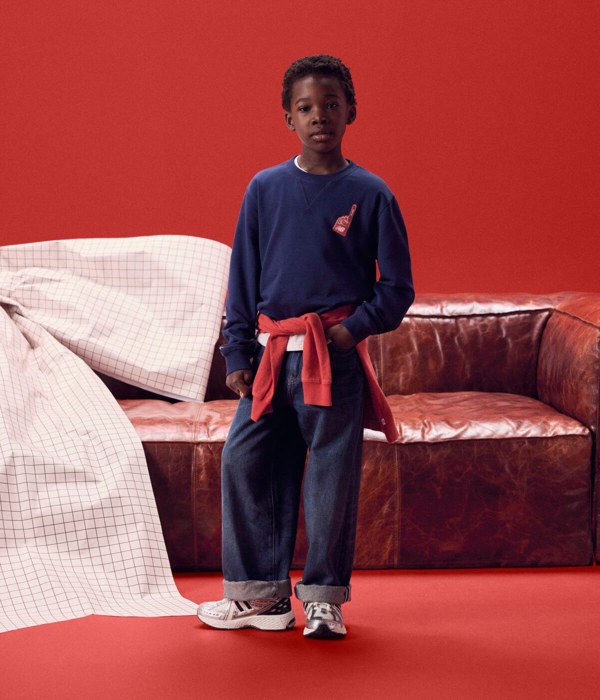 Kid wearing a navy long sleeve shirt in front of a red couch.