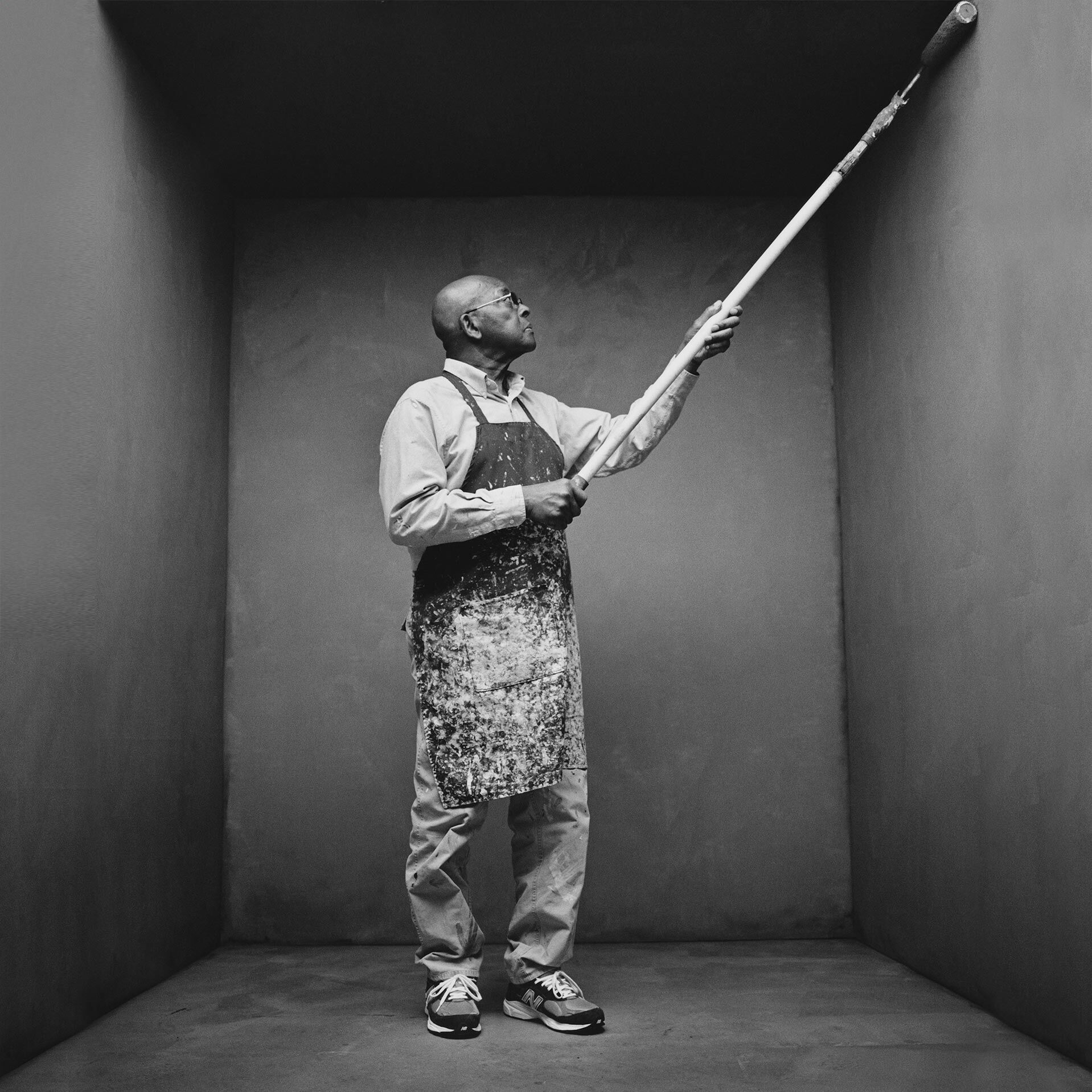 Painter wearing a paid of MADE in US sneakers standing in a concrete studio environment using a roller to paint the backdrop.
